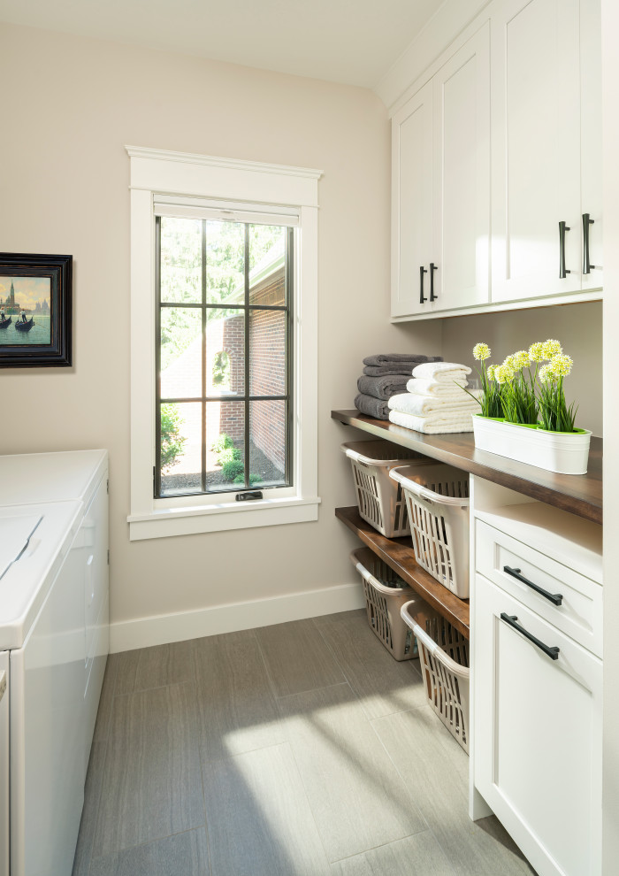 Mid-sized traditional galley dedicated laundry room in Detroit with a drop-in sink, shaker cabinets, white cabinets, wood benchtops, beige walls, porcelain floors, a side-by-side washer and dryer, grey floor and brown benchtop.