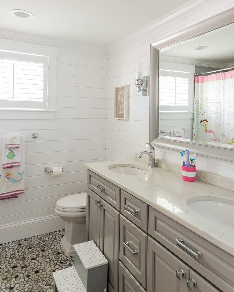 Design ideas for a mid-sized beach style kids bathroom in Boston with raised-panel cabinets, white cabinets, beige tile, white walls, pebble tile floors, an undermount sink, engineered quartz benchtops and grey floor.