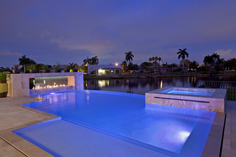 Photo of a large contemporary backyard custom-shaped infinity pool in Miami with a hot tub.