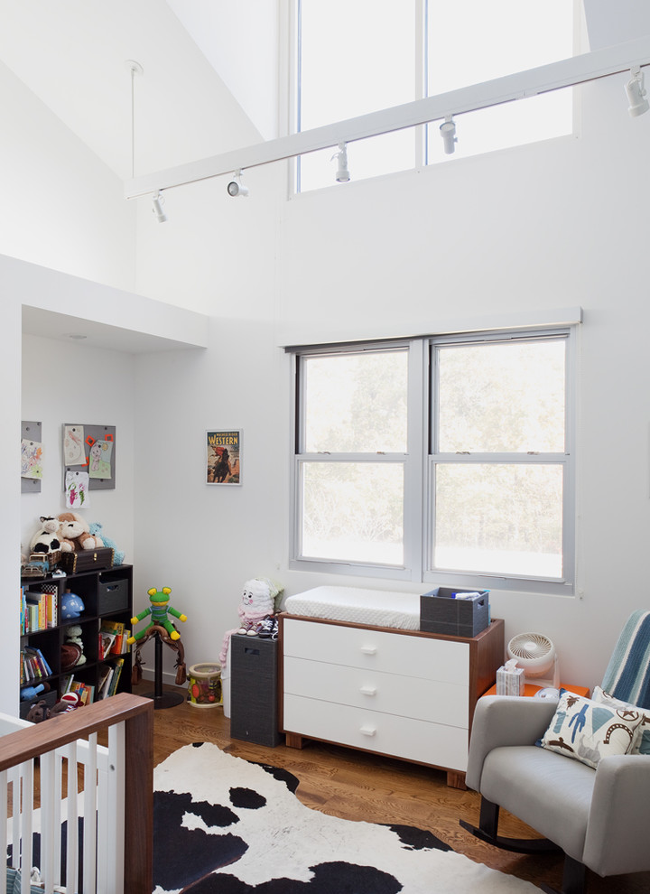 This is an example of a modern gender-neutral nursery in Kansas City with white walls and medium hardwood floors.