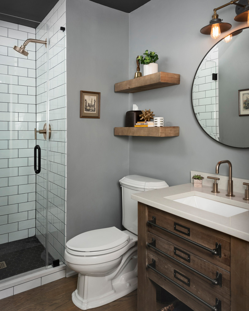 This is an example of a mid-sized industrial 3/4 bathroom in Chicago with medium wood cabinets, a two-piece toilet, white tile, ceramic tile, blue walls, porcelain floors, an undermount sink, engineered quartz benchtops, black floor, a hinged shower door, grey benchtops, a single vanity and a freestanding vanity.