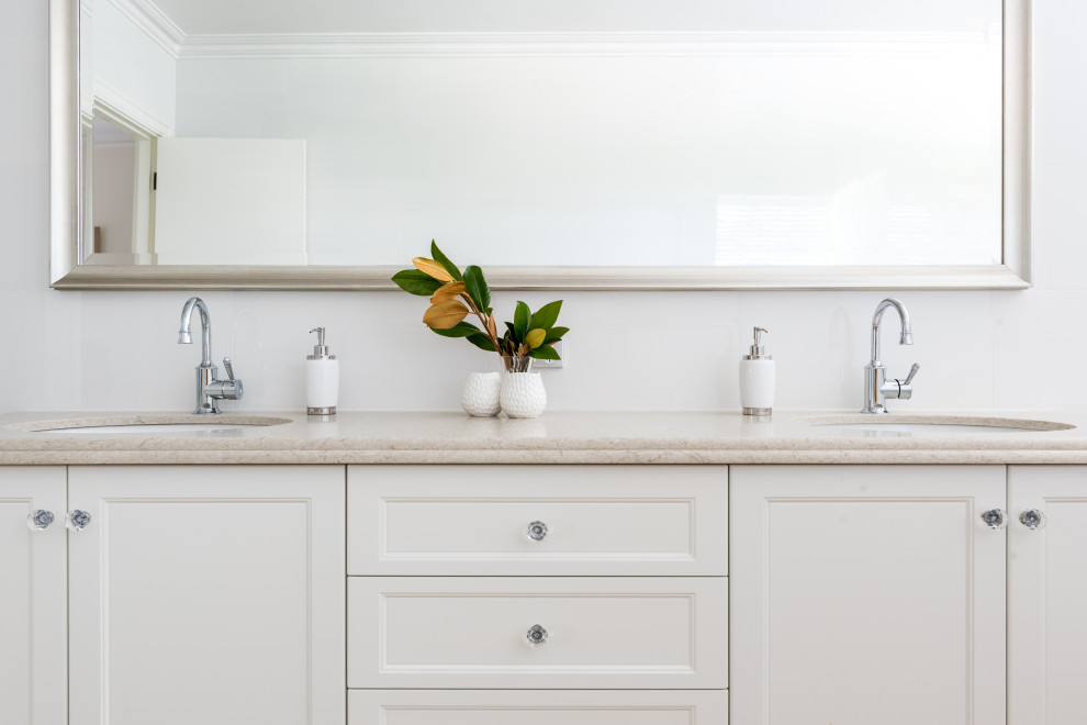 Inspiration for a large beach style 3/4 bathroom in Perth with recessed-panel cabinets, white cabinets, a drop-in tub, white tile, white walls, an undermount sink, beige floor, beige benchtops, a double vanity and a built-in vanity.