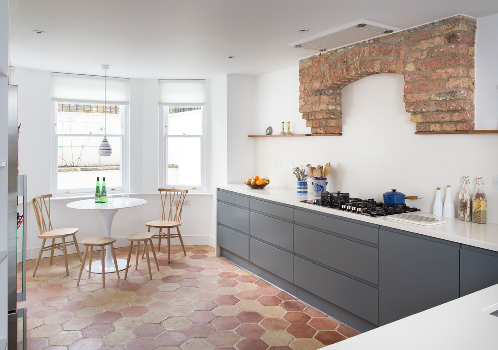 This is an example of a large contemporary l-shaped eat-in kitchen in London with flat-panel cabinets, grey cabinets, stainless steel appliances, terra-cotta floors, a double-bowl sink, solid surface benchtops, white splashback, with island, multi-coloured floor and white benchtop.