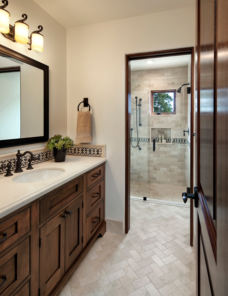 This is an example of a mediterranean bathroom in Santa Barbara with an undermount sink, recessed-panel cabinets, medium wood cabinets, a curbless shower, beige tile, stone tile and beige walls.