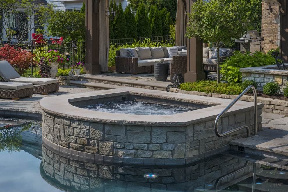 Example of a mid-sized mountain style backyard stone and custom-shaped hot tub design in Chicago