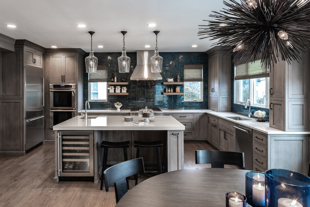 Large country l-shaped eat-in kitchen in Chicago with a single-bowl sink, medium wood cabinets, quartz benchtops, blue splashback, stainless steel appliances, medium hardwood floors, with island, brown floor, grey benchtop, recessed-panel cabinets and ceramic splashback.