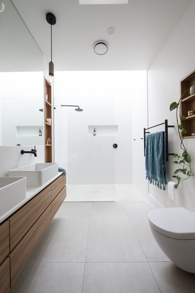 Photo of a contemporary bathroom in Melbourne with flat-panel cabinets, medium wood cabinets, a curbless shower, white tile, white walls, a vessel sink, grey floor, an open shower and white benchtops.