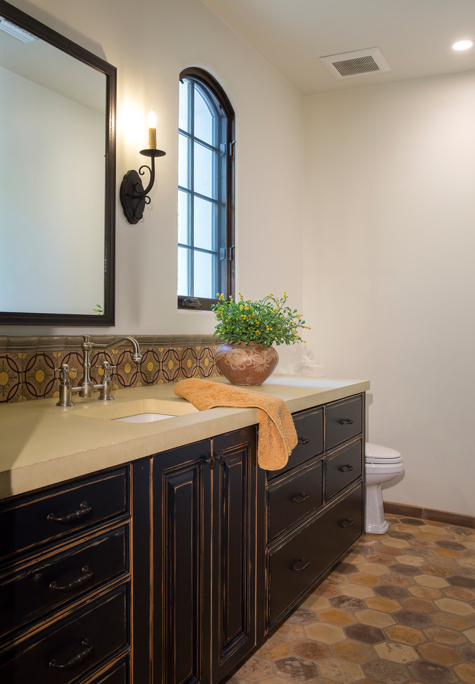 This is an example of a mid-sized mediterranean bathroom in Phoenix with raised-panel cabinets, black cabinets, a two-piece toilet, multi-coloured tile, white walls, terra-cotta floors, an undermount sink, concrete benchtops and multi-coloured floor.