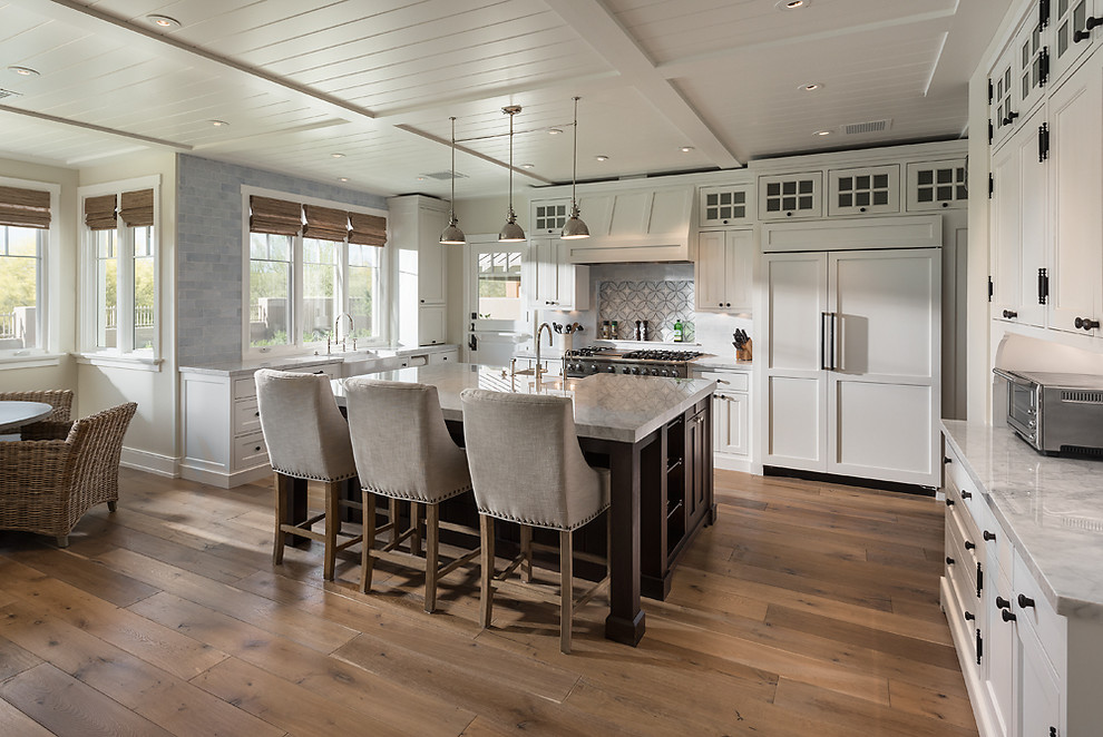Large transitional l-shaped open plan kitchen in Phoenix with a farmhouse sink, raised-panel cabinets, white cabinets, marble benchtops, grey splashback, mosaic tile splashback, stainless steel appliances, medium hardwood floors and with island.
