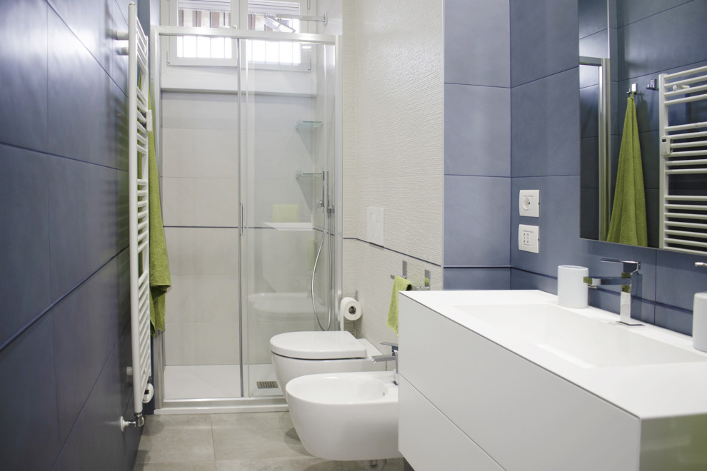 This is an example of a mid-sized contemporary 3/4 bathroom in Milan with flat-panel cabinets, white cabinets, an alcove shower, a wall-mount toilet, blue tile, porcelain tile, blue walls, porcelain floors, an integrated sink, grey floor, a sliding shower screen, a laundry, a single vanity, a floating vanity and recessed.