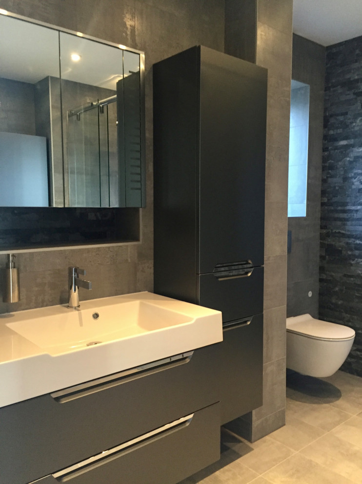 This is an example of a large industrial ensuite wet room bathroom in London with beaded cabinets, black cabinets, a wall mounted toilet, grey tiles, porcelain tiles, grey walls, porcelain flooring, a wall-mounted sink, grey floors, a sliding door, a feature wall, double sinks and a floating vanity unit.