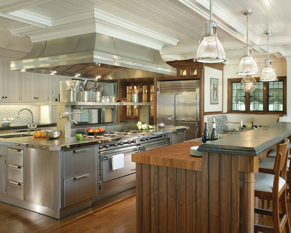 Photo of a traditional eat-in kitchen in New York with flat-panel cabinets, stainless steel cabinets, stainless steel appliances, medium hardwood floors and multiple islands.