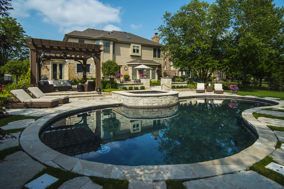 Design ideas for a mid-sized arts and crafts backyard custom-shaped pool in Chicago with a hot tub and natural stone pavers.