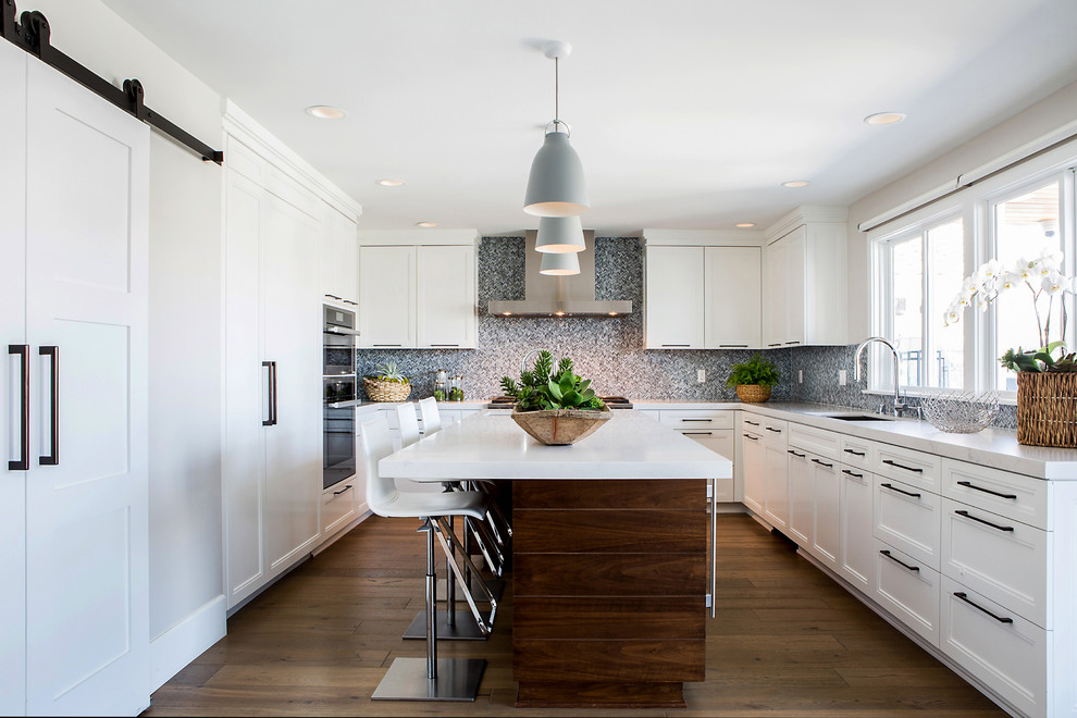 Design ideas for a mid-sized country u-shaped open plan kitchen in Orange County with an undermount sink, shaker cabinets, white cabinets, quartz benchtops, blue splashback, glass tile splashback, stainless steel appliances, medium hardwood floors, with island and brown floor.