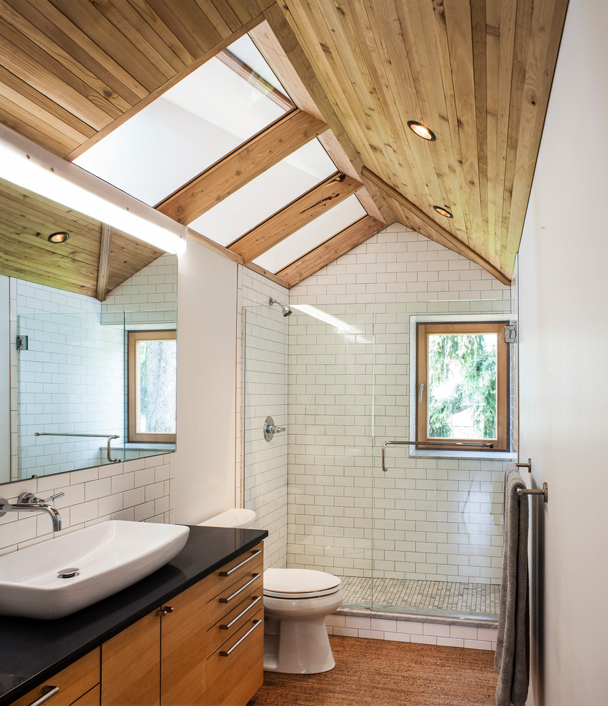This is an example of a contemporary 3/4 bathroom in Portland with flat-panel cabinets, medium wood cabinets, an alcove shower, white tile, subway tile, white walls, a vessel sink, solid surface benchtops, brown floor and a hinged shower door.