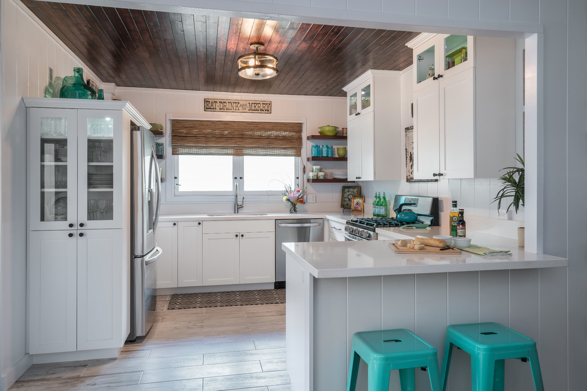 Mid-sized country u-shaped separate kitchen in Hawaii with shaker cabinets, white cabinets, quartz benchtops, stainless steel appliances, an undermount sink, white splashback, timber splashback, porcelain floors, a peninsula and beige floor.