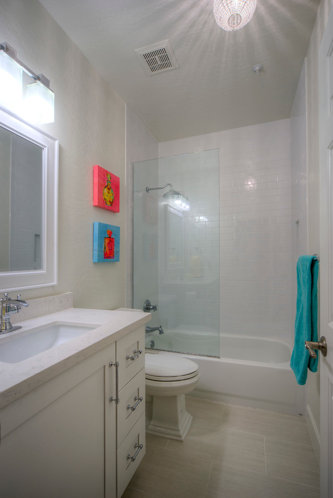 This is an example of a small contemporary kids bathroom in Phoenix with an undermount sink, shaker cabinets, white cabinets, engineered quartz benchtops, a drop-in tub, a shower/bathtub combo, a one-piece toilet, white tile, ceramic tile, grey walls, porcelain floors, beige floor, a sliding shower screen and white benchtops.
