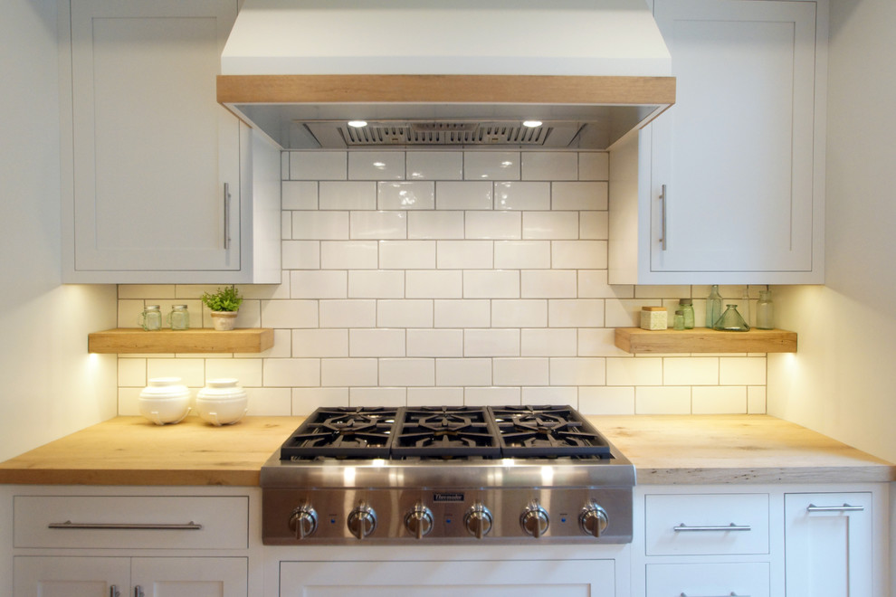 Photo of a mid-sized beach style u-shaped eat-in kitchen in Boston with an undermount sink, shaker cabinets, quartz benchtops, white splashback, subway tile splashback, stainless steel appliances, with island, white benchtop, white cabinets, light hardwood floors and beige floor.