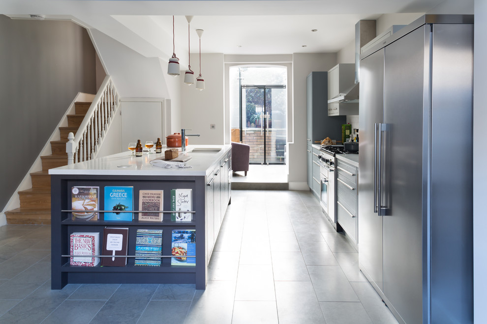 Large traditional galley open plan kitchen in London with an integrated sink, grey cabinets, solid surface benchtops, grey splashback, subway tile splashback, stainless steel appliances and with island.