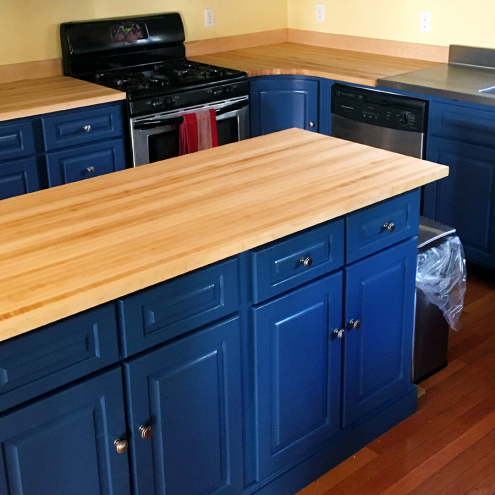 Foto på ett avskilt, stort amerikanskt brun l-kök, med en nedsänkt diskho, luckor med upphöjd panel, blå skåp, träbänkskiva, brunt stänkskydd, stänkskydd i trä, rostfria vitvaror, mellanmörkt trägolv, en köksö och brunt golv