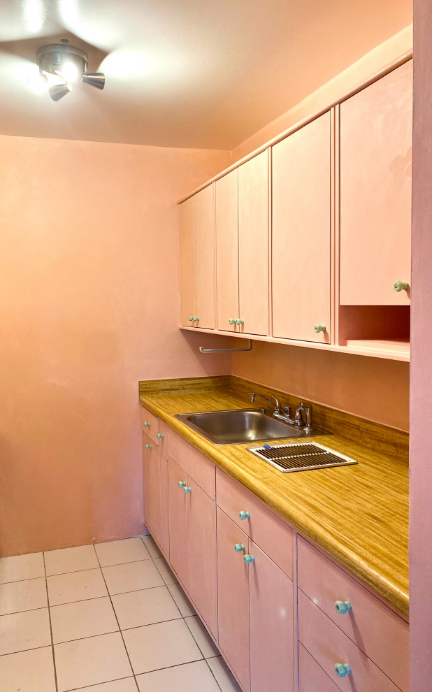 Réalisation d'une cuisine américaine minimaliste de taille moyenne avec un placard à porte plane, des portes de placard rose, une crédence rose, un sol en carrelage de céramique et aucun îlot.