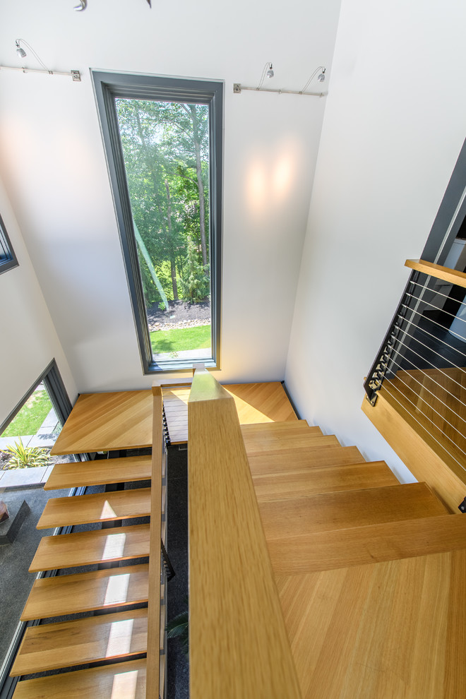 Example of a large minimalist wooden floating open and cable railing staircase design in Cleveland