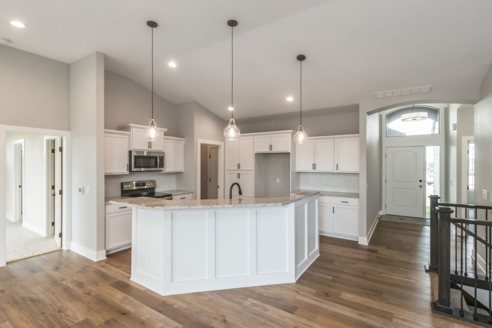 Example of a large transitional u-shaped brown floor and light wood floor kitchen design with an undermount sink, shaker cabinets, white cabinets, quartz countertops, white backsplash, glass tile backsplash, stainless steel appliances, an island and multicolored countertops