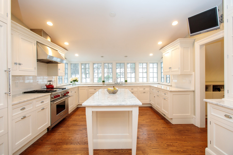 Photo of a large traditional l-shaped open plan kitchen in Boston with a double-bowl sink, recessed-panel cabinets, white cabinets, marble benchtops, white splashback, ceramic splashback, stainless steel appliances, medium hardwood floors and with island.