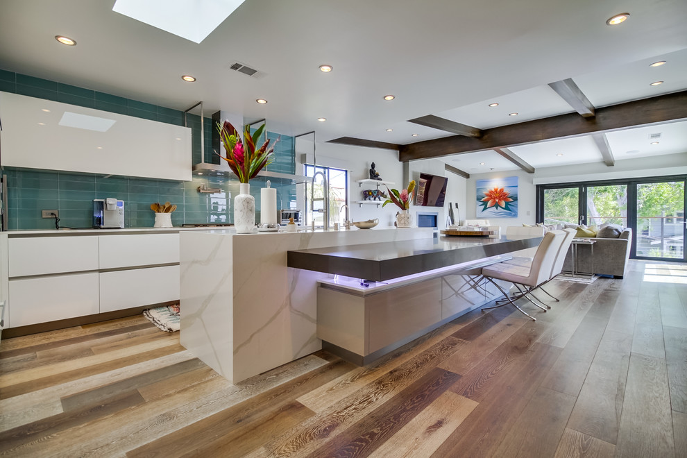Inspiration for a large contemporary open plan kitchen in San Diego with flat-panel cabinets, white cabinets, quartz benchtops, blue splashback, glass tile splashback, medium hardwood floors and with island.