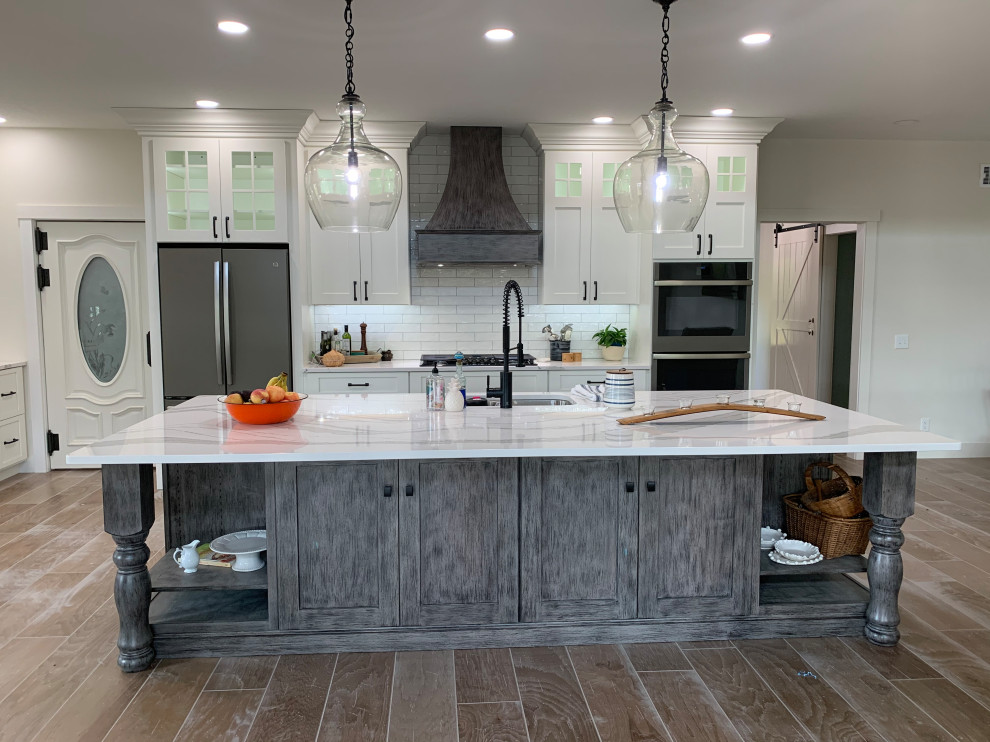 Design ideas for a large rustic l-shaped open plan kitchen in Other with a submerged sink, recessed-panel cabinets, white cabinets, engineered stone countertops, white splashback, stainless steel appliances, an island, brown floors and white worktops.