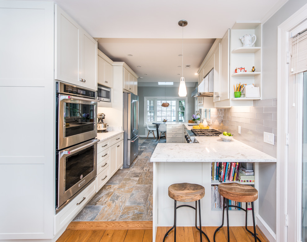 Inspiration for a mid-sized contemporary galley eat-in kitchen in DC Metro with an undermount sink, white cabinets, quartz benchtops, grey splashback, subway tile splashback, stainless steel appliances, slate floors, a peninsula, multi-coloured floor, white benchtop and shaker cabinets.