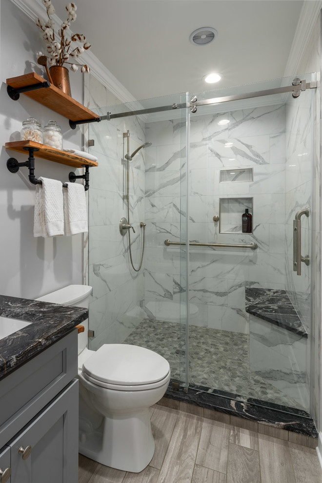 This is an example of a mid-sized transitional master bathroom in Other with shaker cabinets, grey cabinets, an open shower, a two-piece toilet, white tile, porcelain tile, grey walls, porcelain floors, an undermount sink, granite benchtops, grey floor, a sliding shower screen and black benchtops.