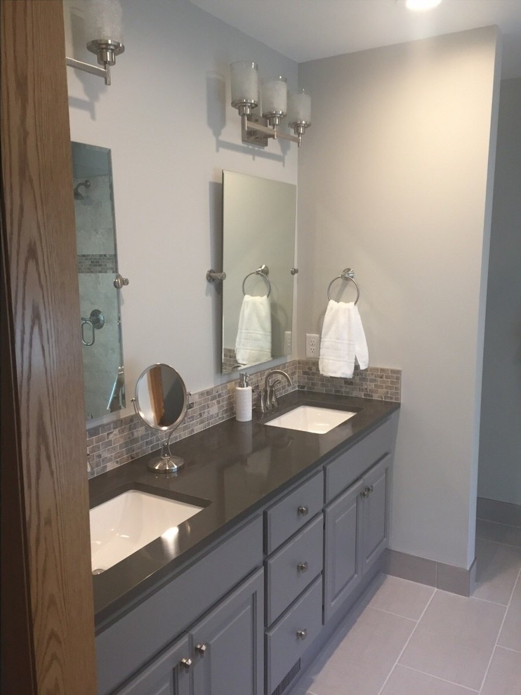 Inspiration for a large transitional master bathroom in Minneapolis with raised-panel cabinets, grey cabinets, a freestanding tub, a corner shower, a two-piece toilet, beige tile, ceramic tile, grey walls, porcelain floors, a drop-in sink, granite benchtops, a hinged shower door and black benchtops.