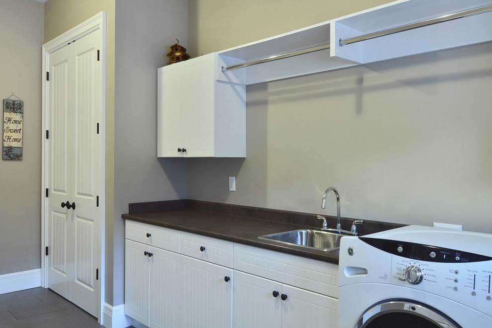 This is an example of a large traditional dedicated laundry room in Vancouver with a drop-in sink, beige walls, white cabinets, soapstone benchtops and a side-by-side washer and dryer.