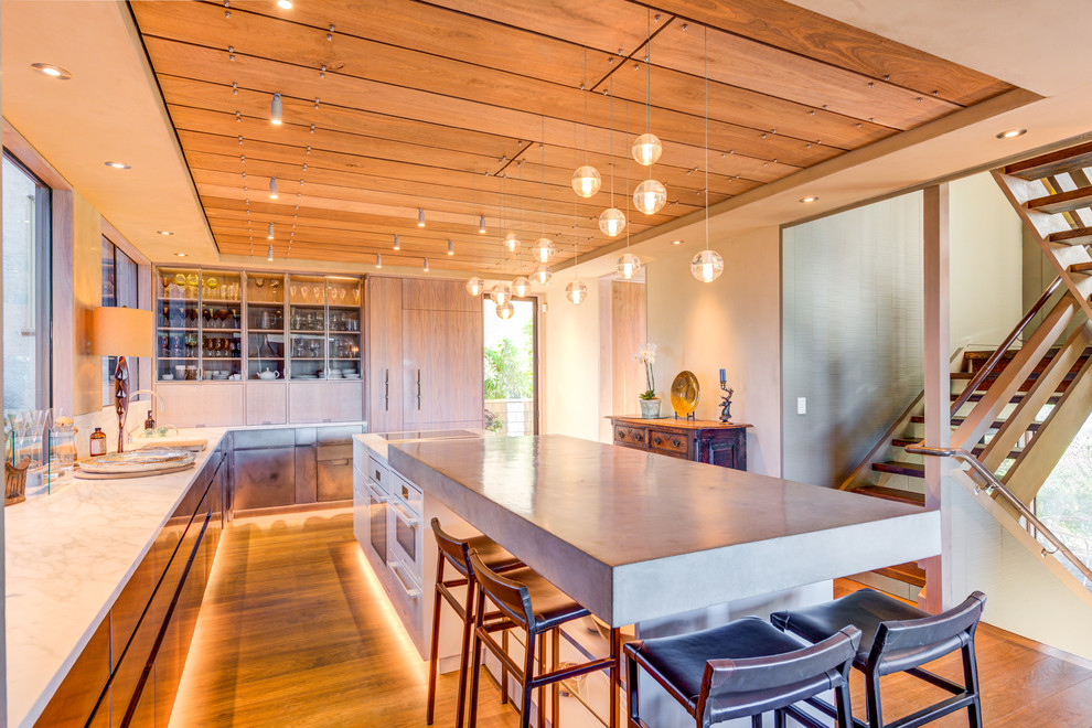 Photo of a contemporary l-shaped kitchen in San Francisco with flat-panel cabinets, medium wood cabinets, concrete benchtops, beige splashback, panelled appliances, medium hardwood floors, with island, brown floor and grey benchtop.