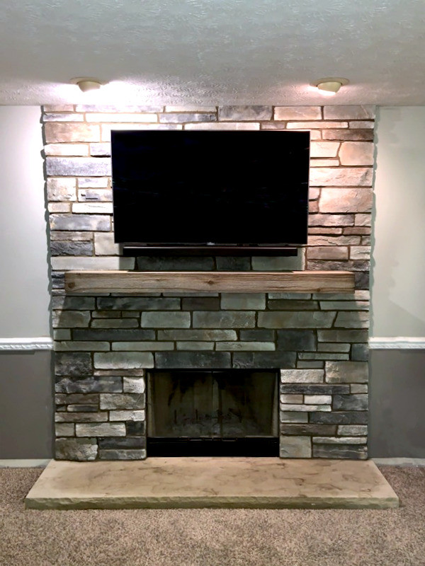 This is an example of a transitional family room in Cleveland with grey walls, a standard fireplace, a stone fireplace surround and a wall-mounted tv.