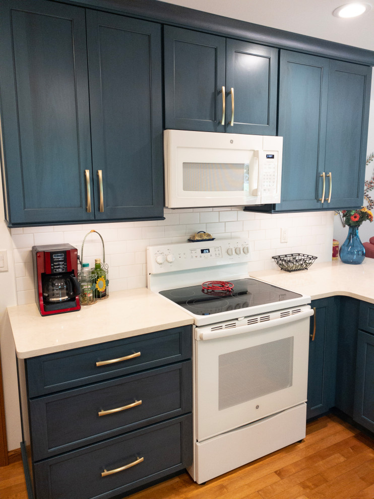 Inspiration for a mid-sized transitional galley light wood floor enclosed kitchen remodel with an undermount sink, flat-panel cabinets, blue cabinets, quartz countertops, white backsplash, subway tile backsplash, white appliances, a peninsula and white countertops