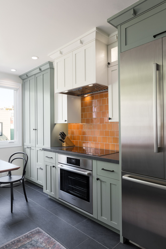 This is an example of an arts and crafts galley eat-in kitchen in San Francisco with an undermount sink, recessed-panel cabinets, green cabinets, quartzite benchtops, orange splashback, stainless steel appliances, ceramic floors, a peninsula, grey floor and black benchtop.