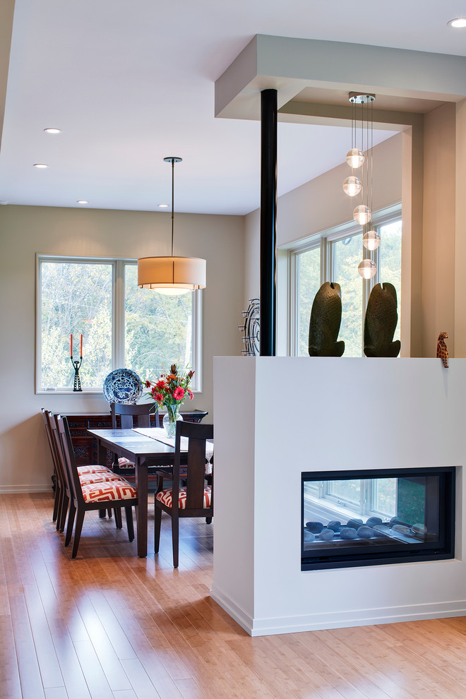 Photo of a mid-sized contemporary open plan dining in Detroit with beige walls, a two-sided fireplace, dark hardwood floors, a plaster fireplace surround and beige floor.