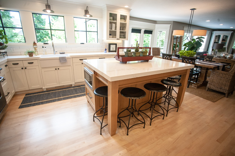 This is an example of a mid-sized transitional l-shaped open plan kitchen in Salt Lake City with a farmhouse sink, shaker cabinets, medium wood cabinets, marble benchtops, white splashback, ceramic splashback, stainless steel appliances, light hardwood floors and with island.