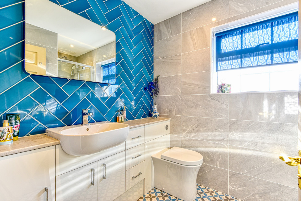 Photo of a mid-sized modern 3/4 bathroom in Sussex with flat-panel cabinets, beige cabinets, an alcove shower, a wall-mount toilet, blue tile, subway tile, beige walls, ceramic floors, a console sink, laminate benchtops, multi-coloured floor, a hinged shower door, beige benchtops, a single vanity and a built-in vanity.
