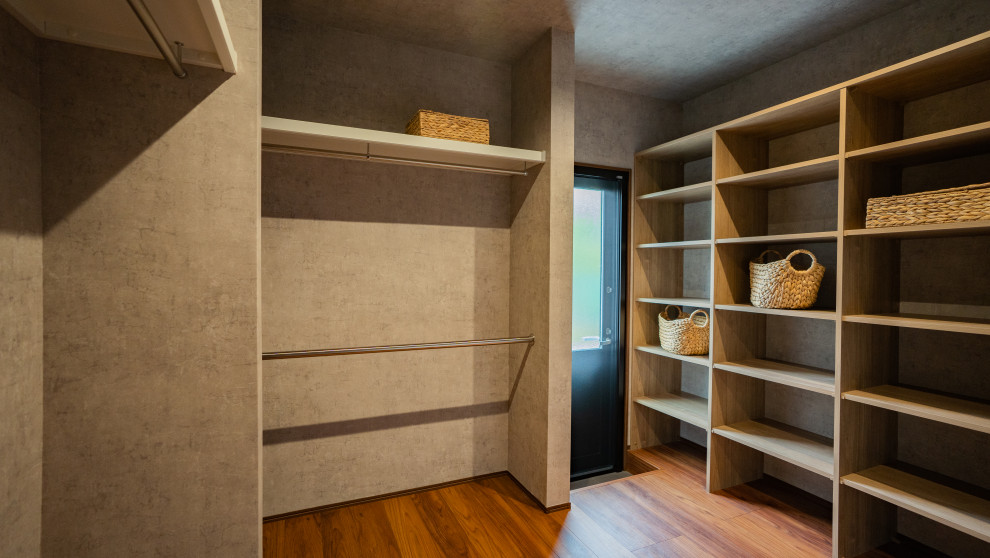 This is an example of an industrial gender-neutral walk-in wardrobe in Other with open cabinets, plywood floors, brown floor, wallpaper and brown cabinets.