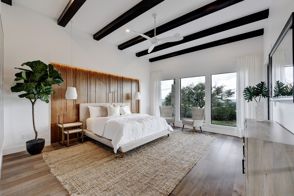 This is an example of a contemporary bedroom in Austin with white walls, medium hardwood floors and brown floor.