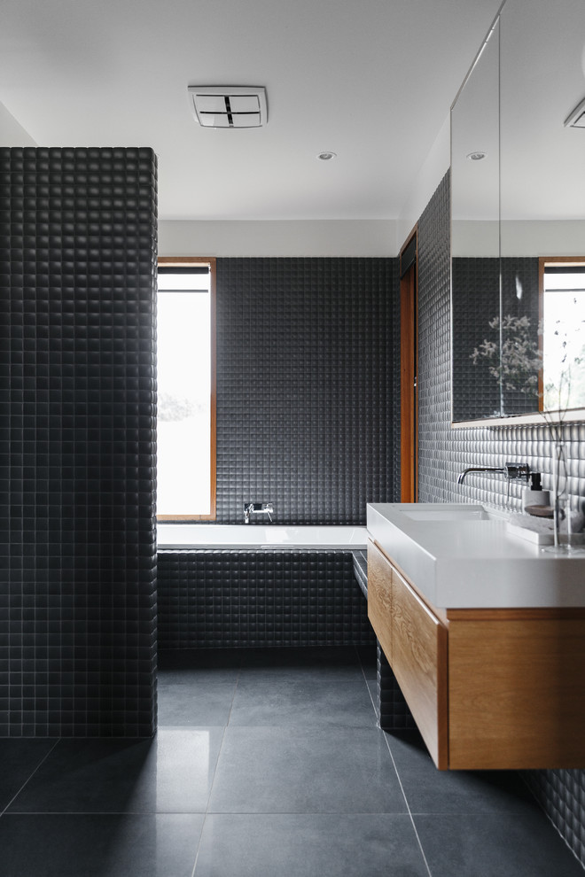 Contemporary bathroom in Adelaide with flat-panel cabinets, medium wood cabinets, a drop-in tub, black tile, black walls, a wall-mount sink and black floor.