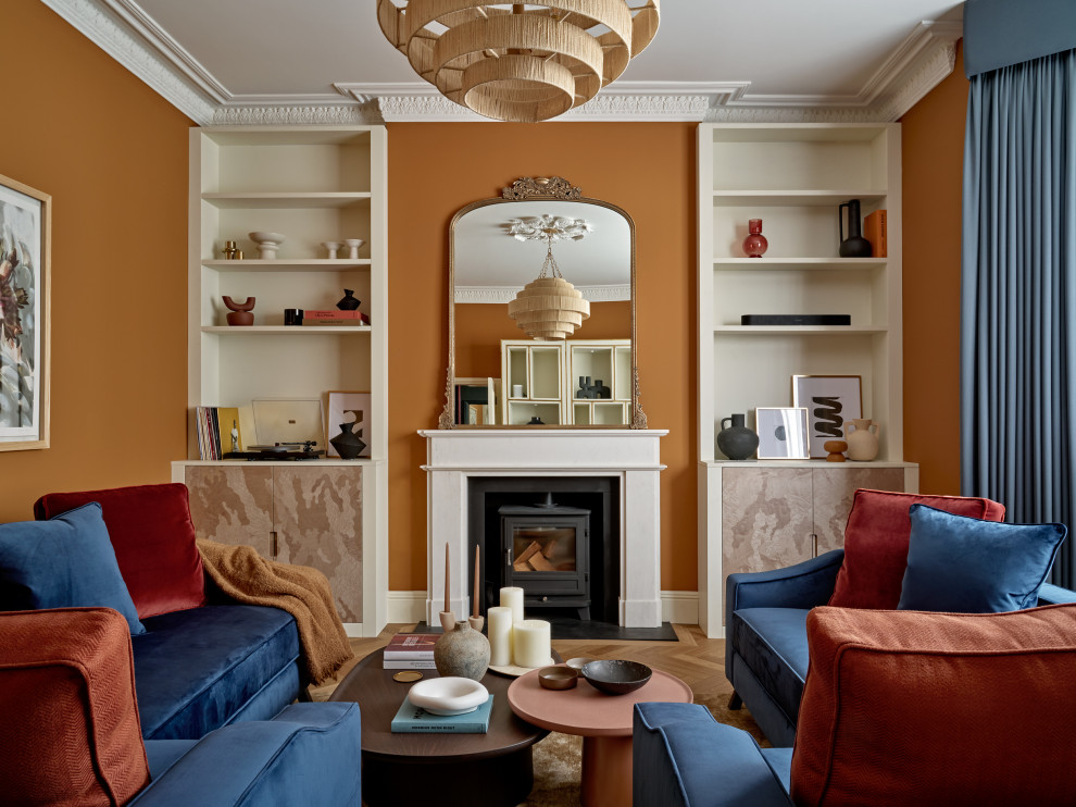 На фото: большая гостиная комната в стиле неоклассика (современная классика) с оранжевыми стенами, печью-буржуйкой, скрытым телевизором, коричневым полом и акцентной стеной с