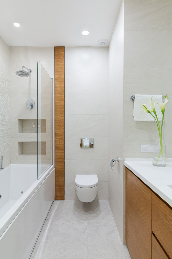 Photo of a small contemporary master bathroom in Saint Petersburg with flat-panel cabinets, medium wood cabinets, a shower/bathtub combo, a wall-mount toilet, beige tile, porcelain tile, porcelain floors, an integrated sink, solid surface benchtops, beige floor, white benchtops and an alcove tub.