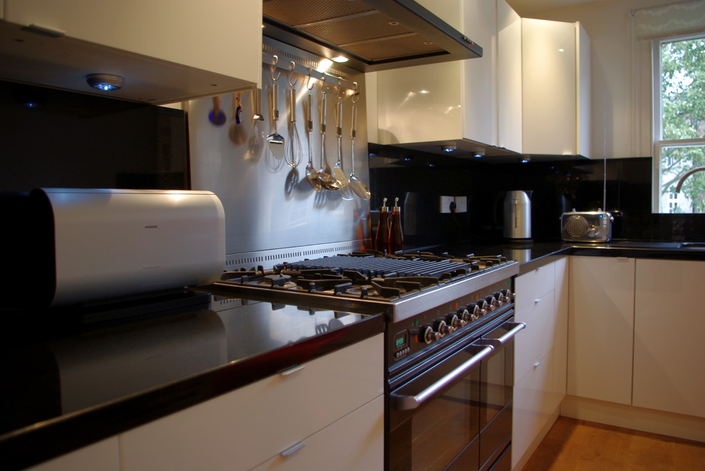 Photo of a mid-sized modern l-shaped separate kitchen in London with an integrated sink, flat-panel cabinets, white cabinets, granite benchtops and stainless steel appliances.