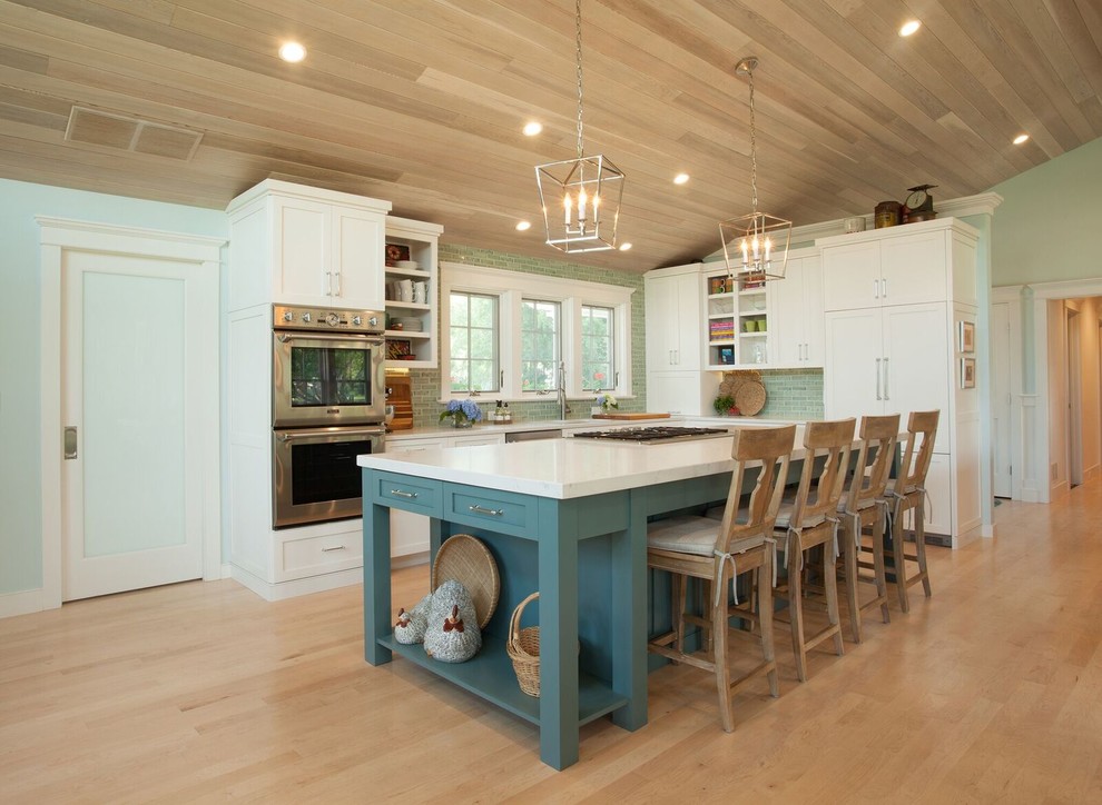 Photo of a beach style l-shaped kitchen in Providence with shaker cabinets, white cabinets, green splashback, subway tile splashback, stainless steel appliances, light hardwood floors, with island, beige floor and white benchtop.