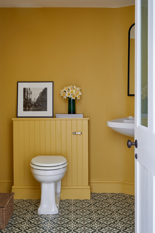 Пример оригинального дизайна: туалет в классическом стиле с желтыми стенами, полом из керамической плитки, разноцветным полом и подвесной тумбой