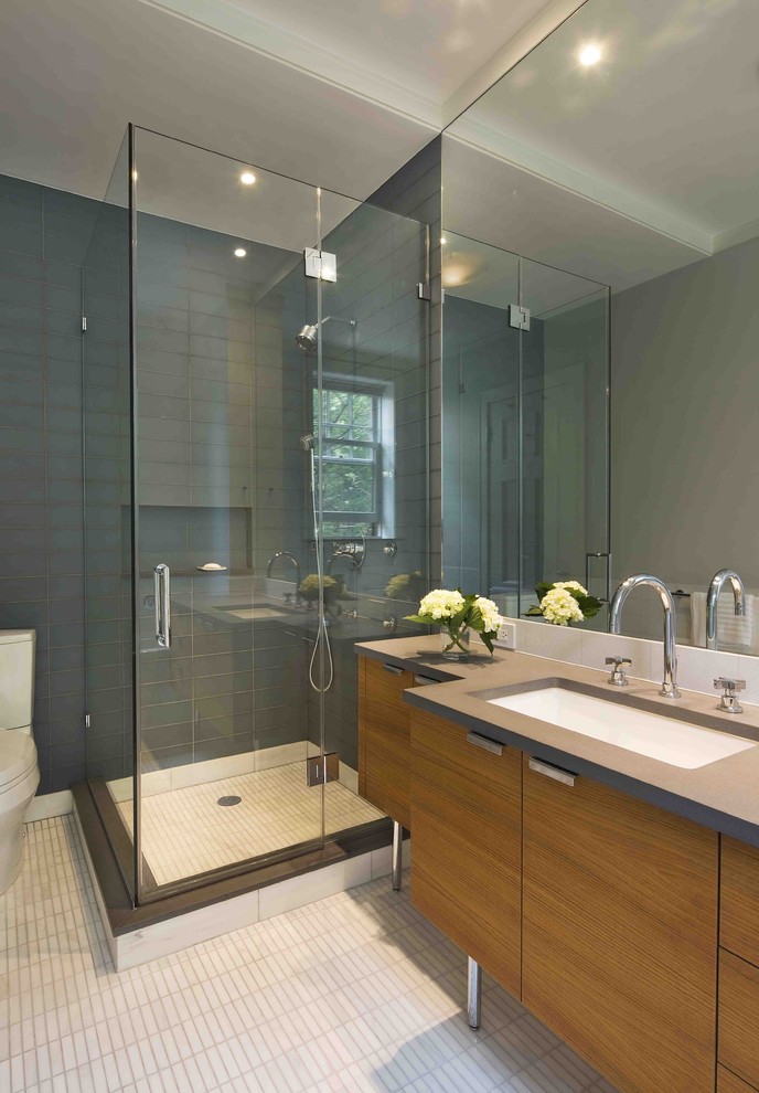 Photo of a modern bathroom in New York with an undermount sink, flat-panel cabinets, medium wood cabinets, a two-piece toilet and gray tile.